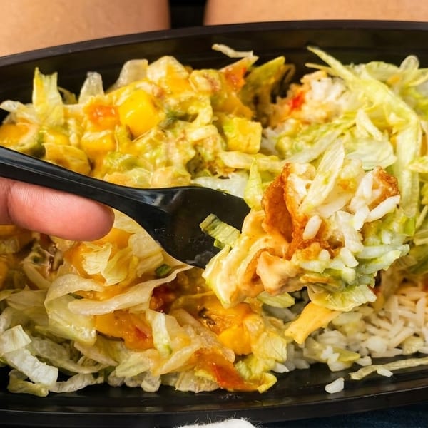 A hand holding a black fork, scooping up a bite of a rice bowl with lettuce and sauce.