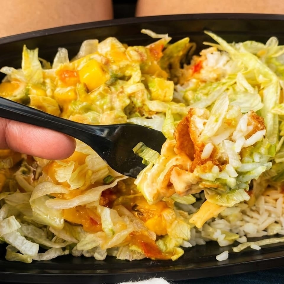 A hand holds a black fork, scooping up a bite of a rice bowl with lettuce and mango salsa.