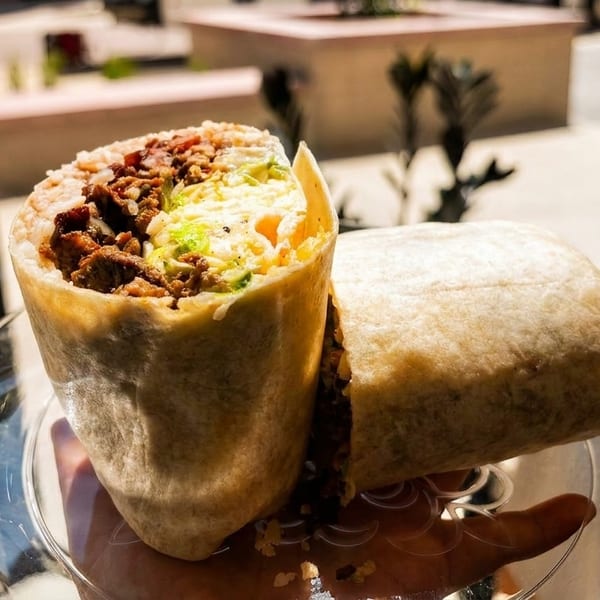 A large, cut burrito filled with meat, rice, and avocado, held on a clear plate.