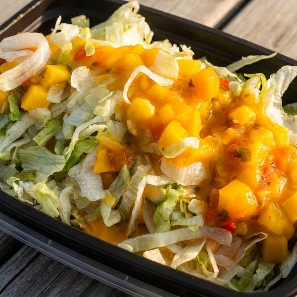 Takeout container filled with shredded lettuce and topped with mango salsa and shrimp.